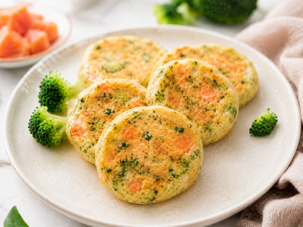 Baby Pancakes mit Lachs und Brokkoli auf einem Teller, daneben Brokkoliröschen und Lachswürfel